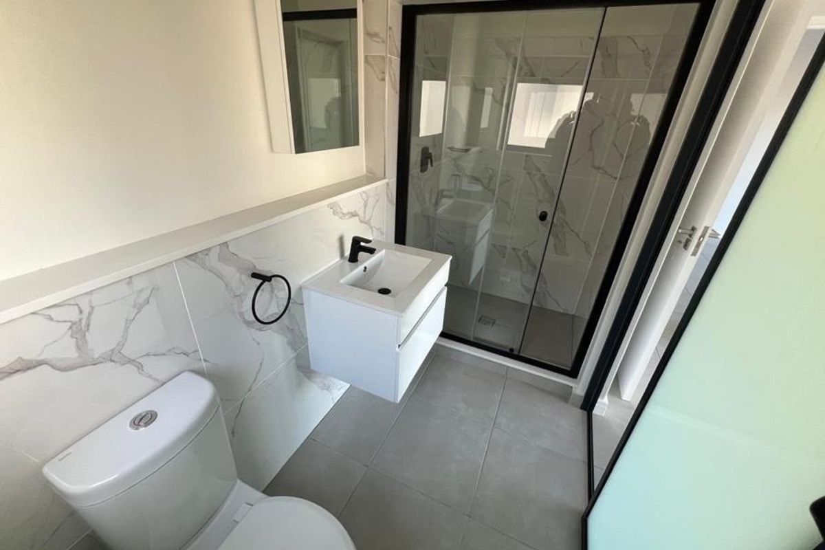 Modern bathroom featuring a wall-mounted vanity, walk-in shower with black-framed glass screen, and elegant marble-look wall tiling.