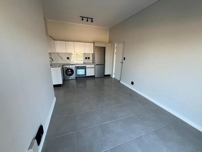 Modern open-plan kitchen and living area featuring sleek cabinetry, integrated appliances, and neutral tiled flooring in a clean, well-maintained space.