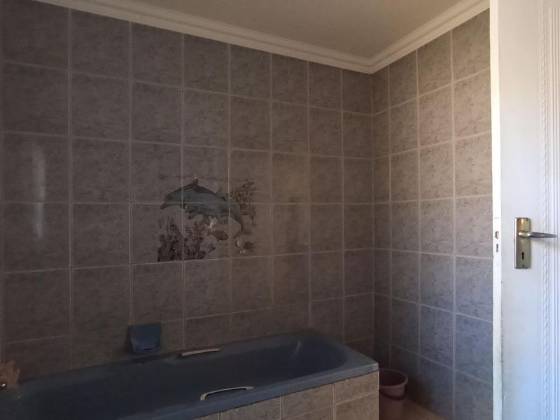 A functional bathroom featuring full-height wall tiling, a built-in bathtub, and classic coving, offering a blank canvas for modern renovation.