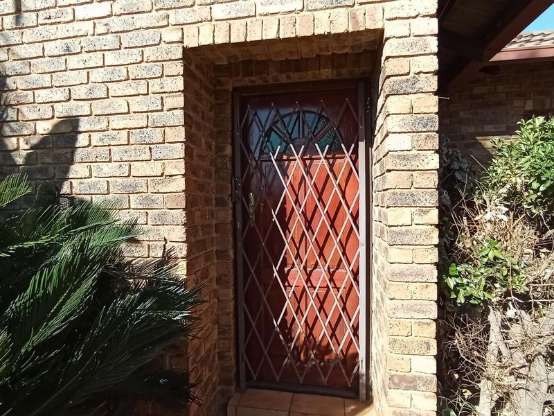 A secure entrance featuring a solid door protected by a metal security gate, set within a classic face brick exterior wall.
