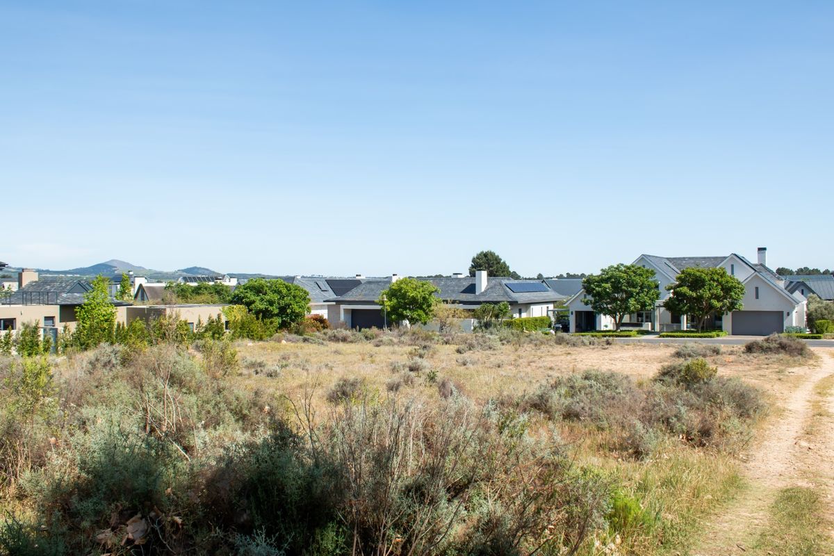 A view of a vacant residential plot with surrounding established homes and distant mountain scenery.