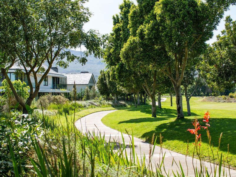 A beautifully landscaped garden area featuring a winding paved walkway, lush green lawns, and mature trees, providing a serene outdoor environment.