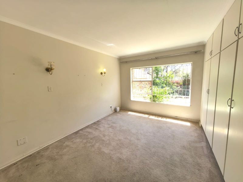 A spacious, empty bedroom featuring built-in cupboards, carpeted flooring, and large windows with security bars, offering a blank canvas for personalization.