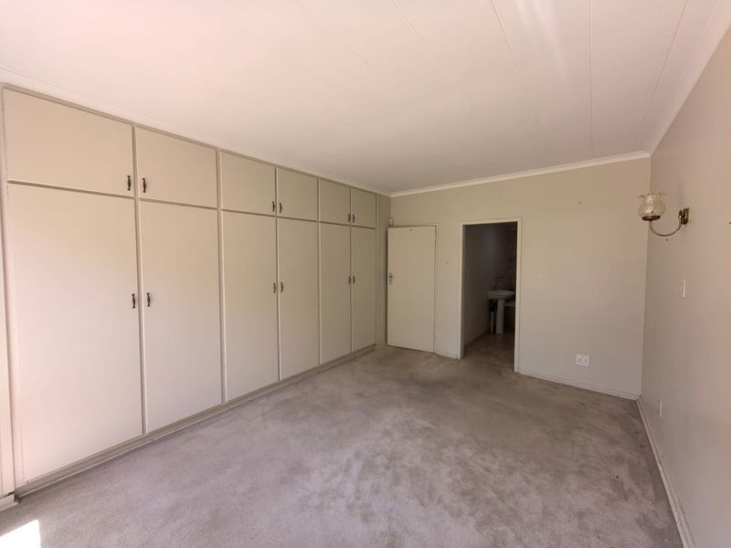 A spacious, empty bedroom featuring extensive built-in cupboards, neutral wall tones, and carpeted flooring, offering a blank canvas for personalization.