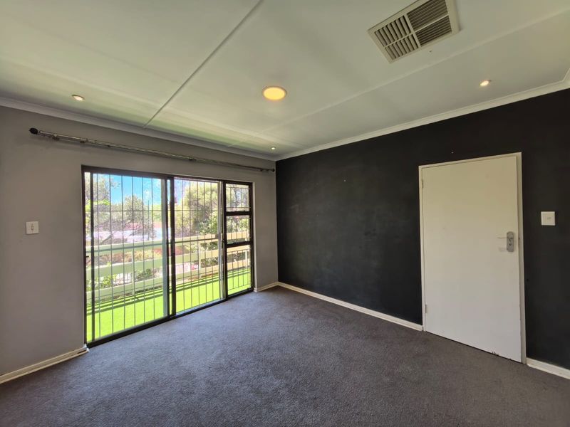 An empty bedroom featuring grey carpet, a dark accent wall, and a sliding glass door with security bars leading to an outdoor area.