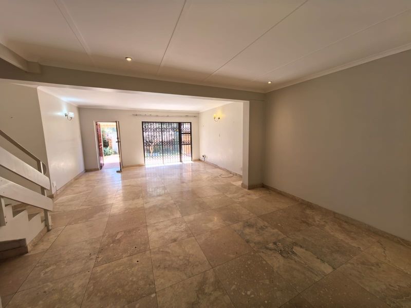 Spacious, empty living area featuring stone tile flooring, recessed lighting, and direct access to an outdoor patio through a security gate.