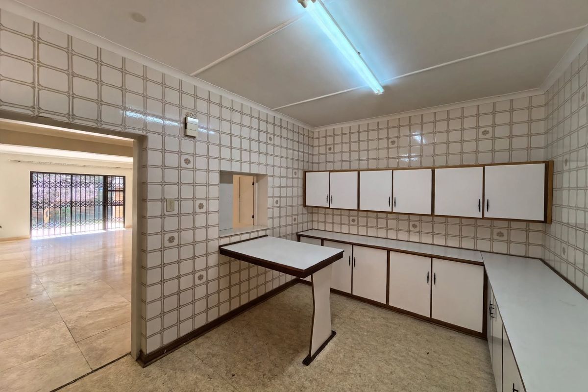 A dated, empty kitchen featuring extensive wall tiling, built-in cabinetry, and a convenient serving hatch connecting to the adjacent living area.