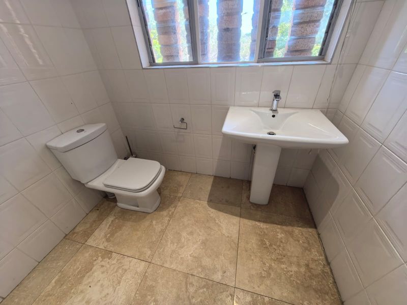 A functional bathroom featuring a pedestal basin, toilet, and tiled finishes throughout, providing a clean and simple layout.