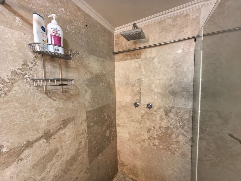 A walk-in shower featuring natural stone wall tiling, a modern rain shower head, and a glass enclosure.
