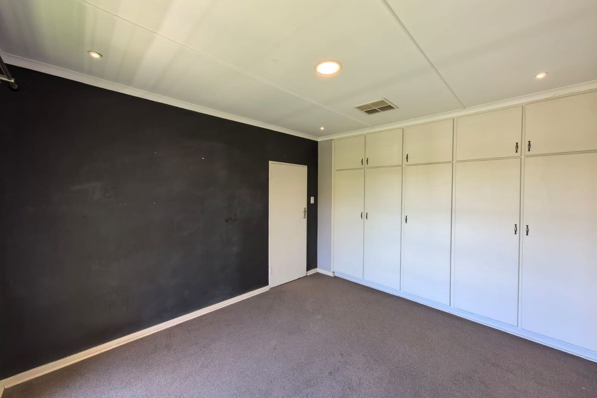 Spacious bedroom featuring a dark accent wall, neutral carpeting, and extensive built-in cupboard storage with recessed lighting.