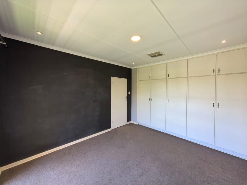 Spacious bedroom featuring a dark accent wall, neutral carpeting, and extensive built-in cupboard storage with recessed lighting.
