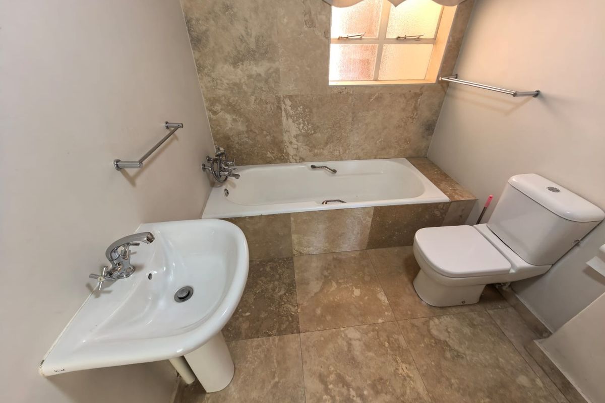 A clean bathroom featuring a built-in bathtub with travertine tiling, a pedestal basin, and a standard toilet, finished with chrome fixtures.