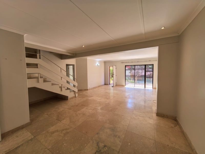 Spacious open-plan living area featuring neutral stone floor tiles, a built-in staircase, and direct access to the outdoor area through a security gate.