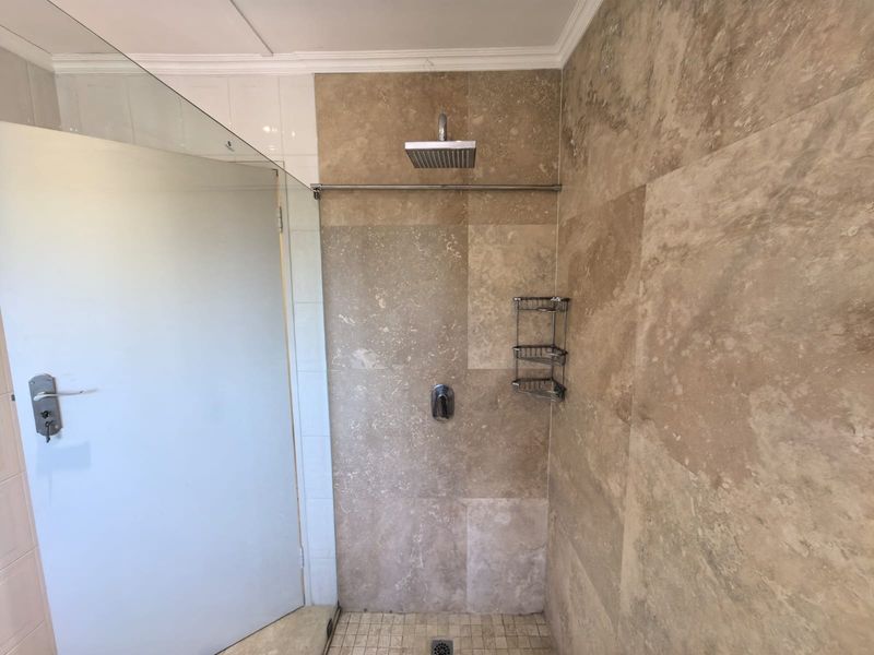 A modern walk-in shower featuring a rain shower head, glass screen, and natural stone wall tiling.