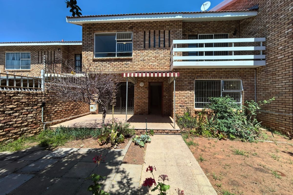 Rear view of a face brick townhouse featuring a paved patio, a balcony, and a small garden area with security features.
