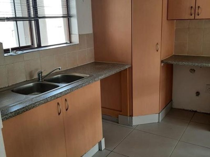 A functional kitchen space featuring laminate cabinetry, double bowl sink, tiled splashbacks, and tiled flooring, offering a blank canvas for potential modern updates.