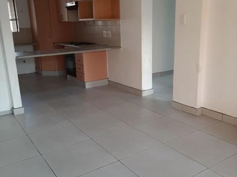 An open-plan living and kitchen area featuring tiled flooring, built-in cabinetry, and a breakfast counter, offering a functional and versatile space.