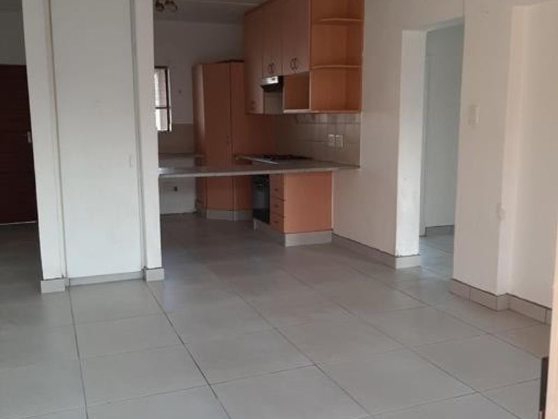 An open-plan living and kitchen area featuring tiled flooring and built-in cabinetry with an integrated oven and hob.