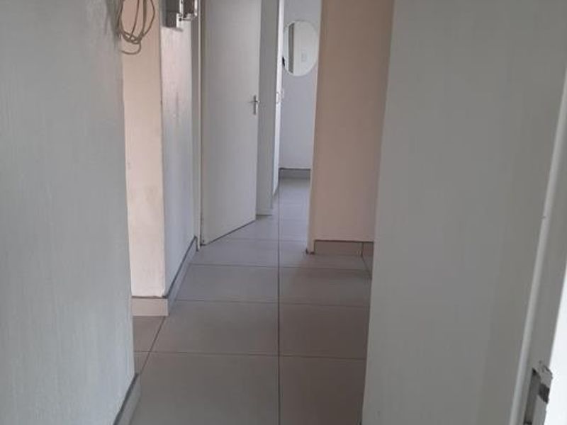 A simple, tiled hallway connecting multiple rooms, featuring neutral walls and standard internal doors.