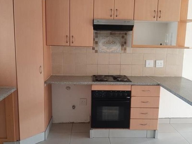 A functional kitchen featuring light wood-tone cabinetry, a built-in oven with hob, and tiled flooring. The space is vacant and ready for updates.