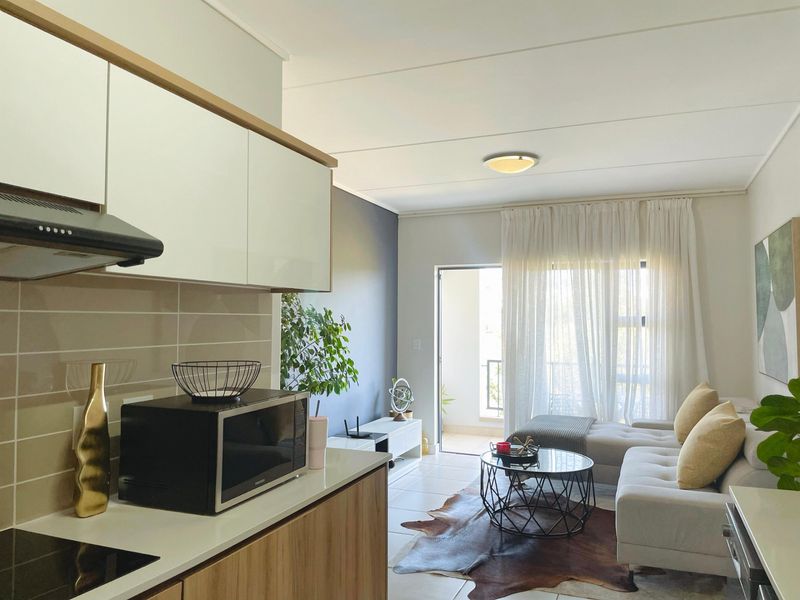 Modern open-plan living area featuring a contemporary kitchen with sleek cabinetry and a seamless transition to a bright balcony through sliding glass doors.