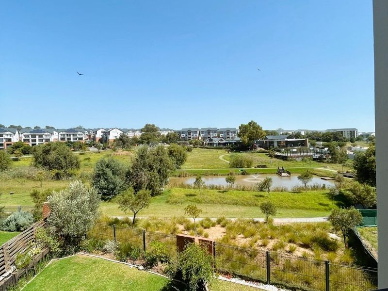 A scenic elevated view overlooking a landscaped estate garden, pond, and surrounding residential complex from a private balcony.