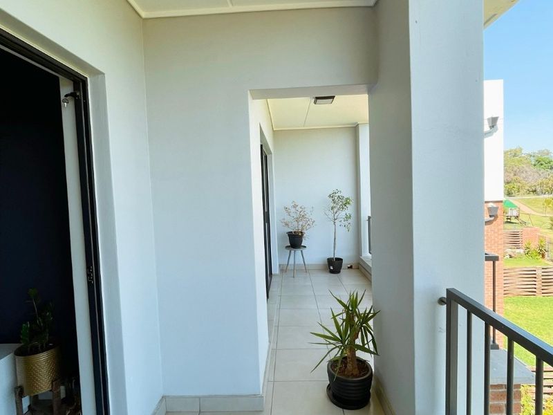 A clean, covered balcony featuring tiled flooring and a metal balustrade, offering an open outdoor space accessible from the interior living area.