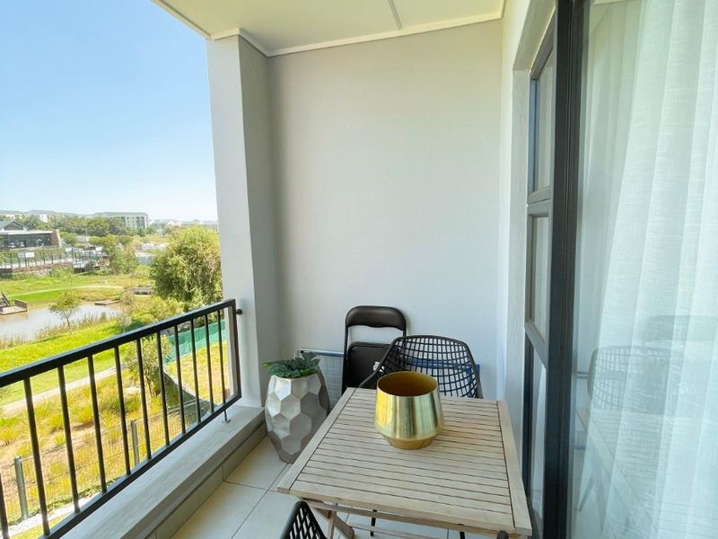 A covered balcony featuring tiled flooring, a metal balustrade, and sliding glass door access, offering pleasant views of the surrounding landscape.