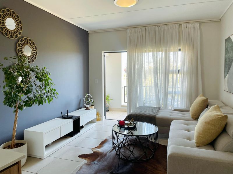 A bright and modern living room featuring tiled flooring and a sliding glass door that opens onto a private balcony.