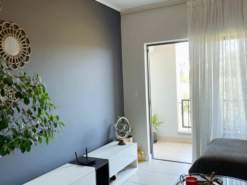 A modern living room featuring neutral tiled flooring, a dark accent wall, and a sliding glass door providing access to an outdoor balcony area.