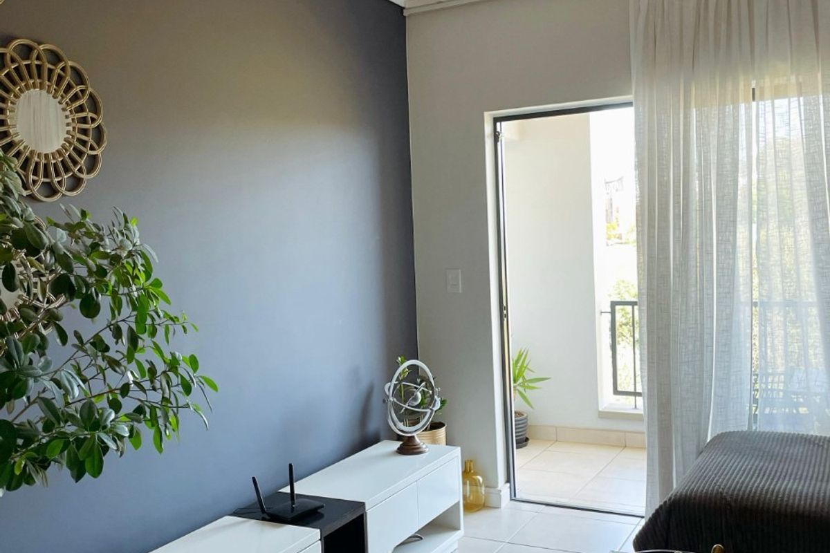 A modern living room featuring neutral tiled flooring, a dark accent wall, and a sliding glass door providing access to an outdoor balcony area.