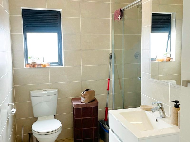 A modern bathroom featuring neutral wall and floor tiles, a white vanity with basin, and a glass-enclosed shower.
