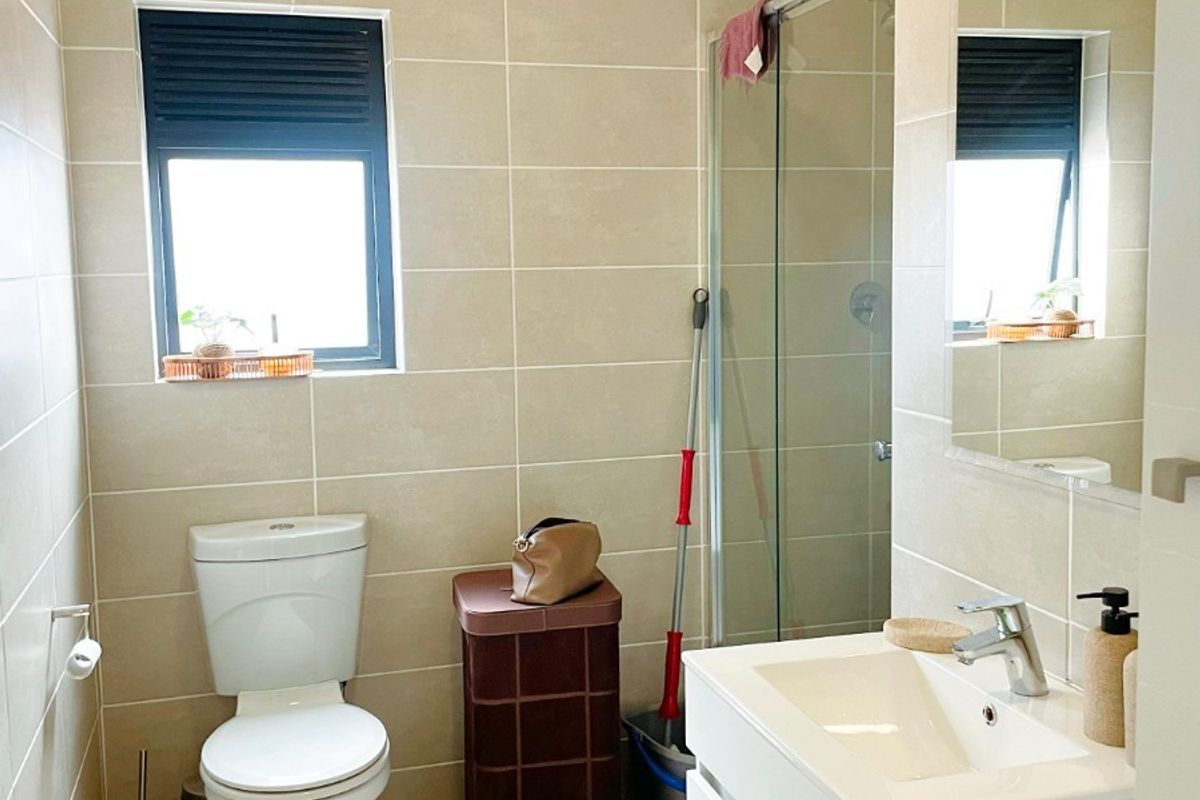 A modern bathroom featuring neutral wall and floor tiles, a white vanity with basin, and a glass-enclosed shower.