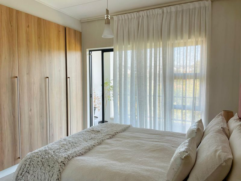 A well-lit bedroom featuring floor-to-ceiling built-in wooden wardrobes and a sliding door providing access to an outdoor balcony area.
