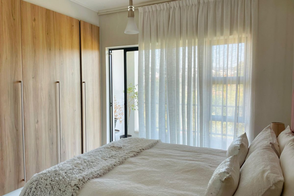 A well-lit bedroom featuring floor-to-ceiling built-in wooden wardrobes and a sliding door providing access to an outdoor balcony area.
