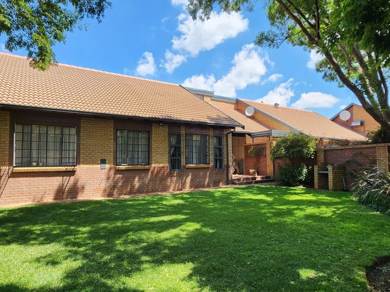 Rear view of the townhouse featuring a brick facade, tiled roof, and a private garden with a built-in braai area.
