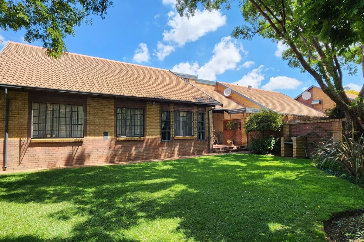 Rear view of the townhouse featuring a brick facade, tiled roof, and a private garden with a built-in braai area.