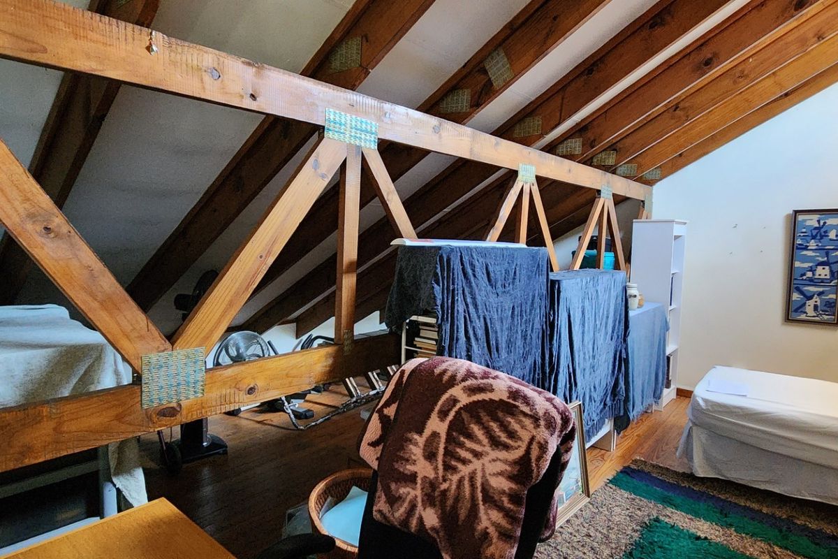 Attic-style bedroom featuring exposed timber roof trusses, pitched ceilings, and warm timber flooring, offering a unique and character-filled living space.