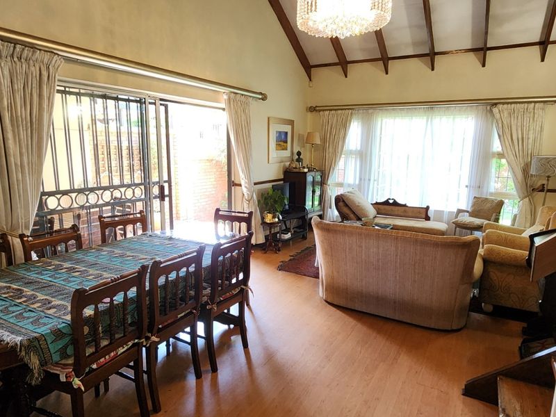 Spacious open-plan living and dining area featuring vaulted ceilings with exposed timber beams, laminate flooring, and direct access to an outdoor patio.