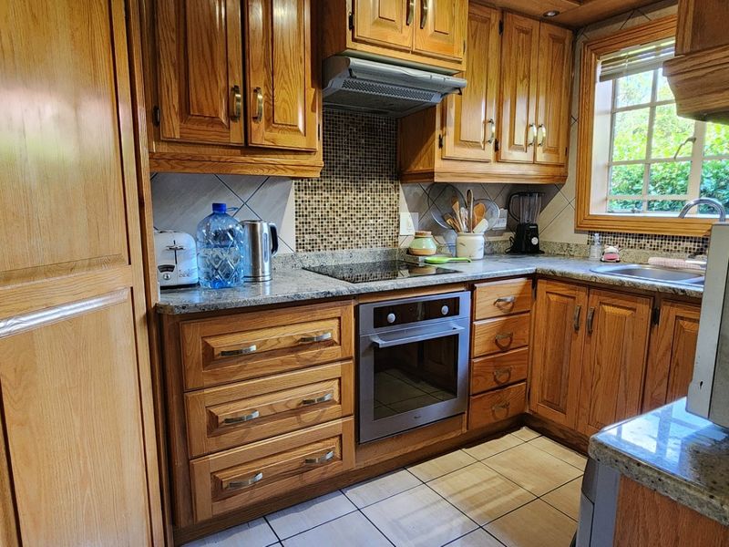A functional kitchen featuring traditional wooden cabinetry, granite countertops, a mosaic tile backsplash, and integrated cooking appliances.