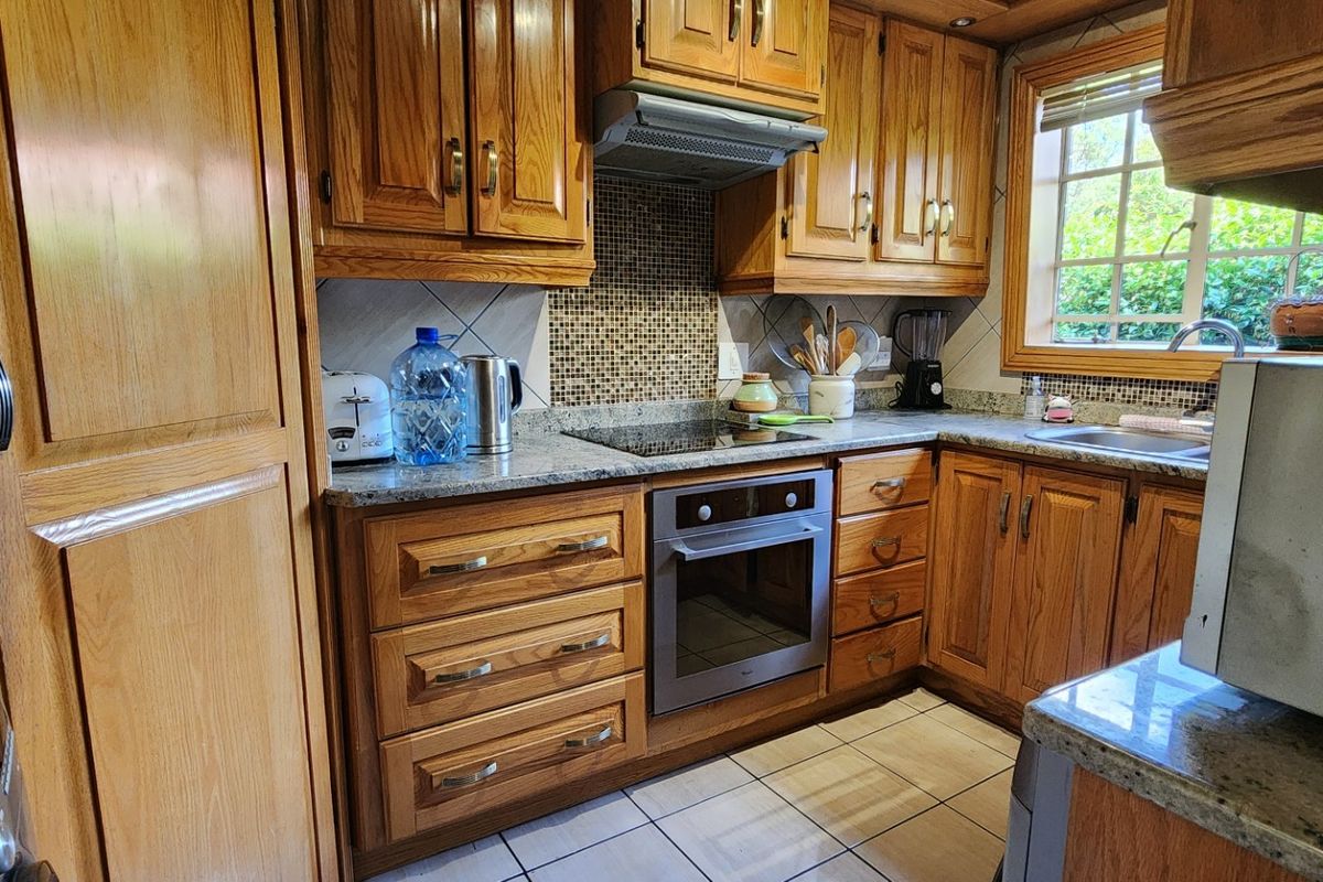 A functional kitchen featuring traditional wooden cabinetry, granite countertops, a mosaic tile backsplash, and integrated cooking appliances.