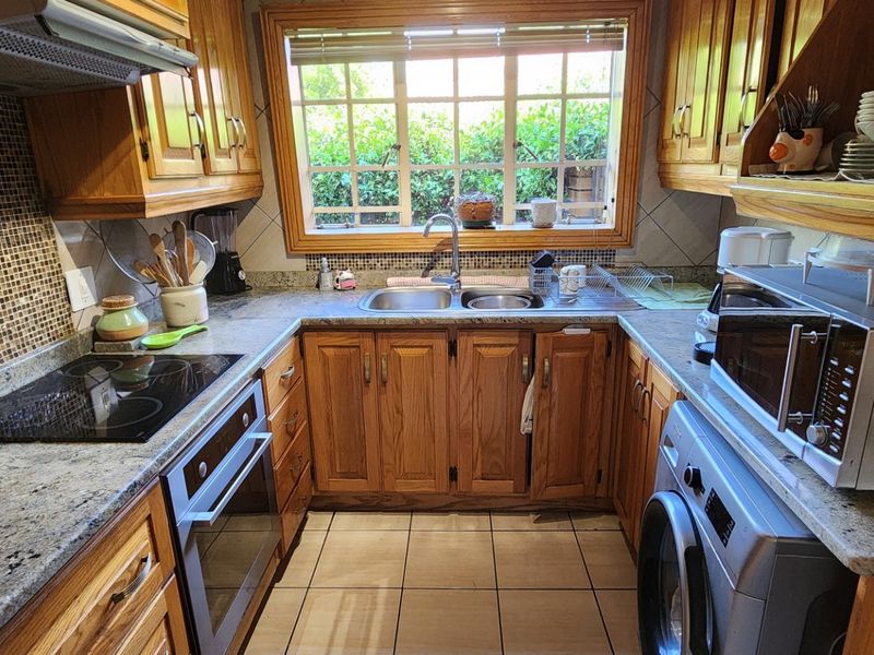 A functional kitchen featuring warm wooden cabinetry, granite countertops, mosaic tile backsplash, and integrated appliances including an oven, hob, and laundry connection.