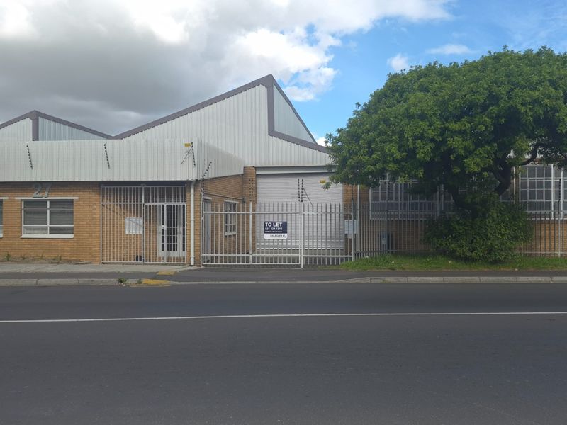 Front elevation of an industrial property featuring brick construction, metal roofing, secure perimeter fencing, and a roller shutter door access point.