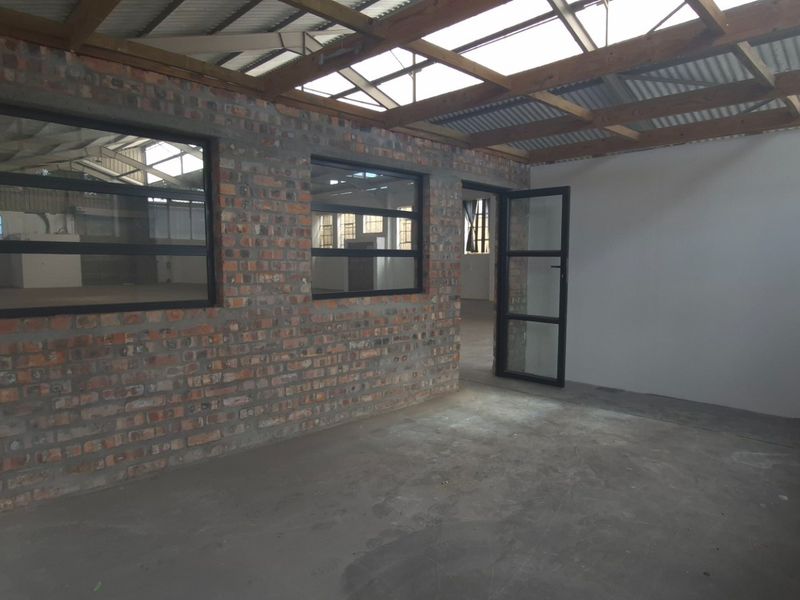 An industrial-style utility space featuring exposed brick walls, timber roof trusses with skylights, and steel-framed windows, offering a versatile open-plan layout.