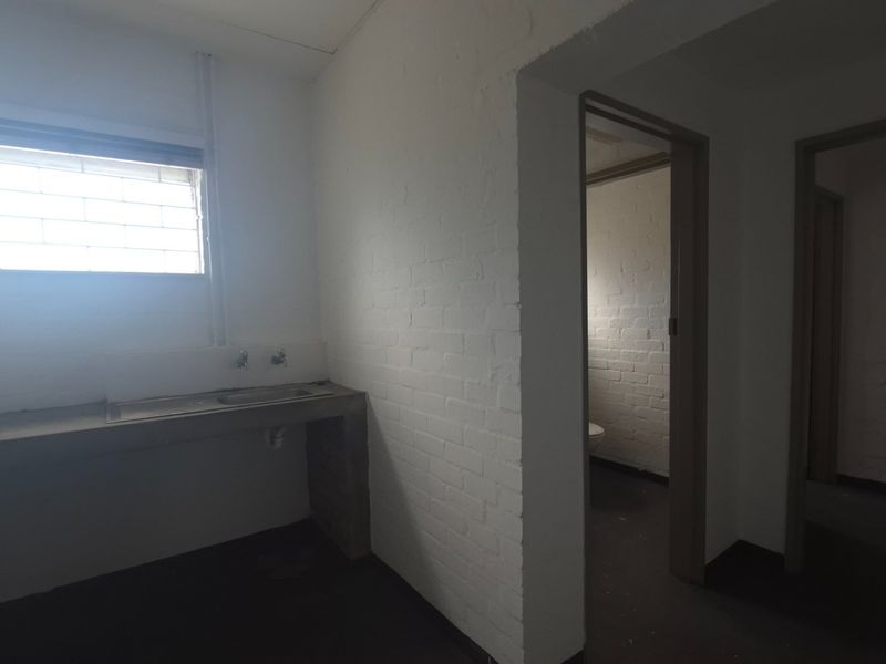 A functional utility space featuring a concrete sink, security-barred window, and exposed brick walls, providing a basic area for industrial or service-related tasks.