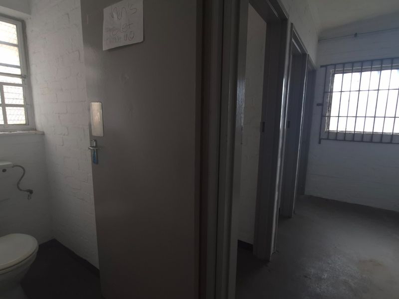 Industrial style communal bathroom facility featuring painted brick walls, security barred windows, a toilet, and a wall-mounted basin.