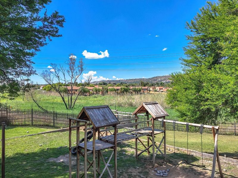 A spacious communal garden area featuring mature trees, manicured lawn, and perimeter fencing with views of the surrounding neighborhood.