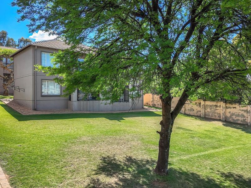 Rear view of the apartment building featuring a spacious lawn, paved walkways, and a perimeter boundary wall.
