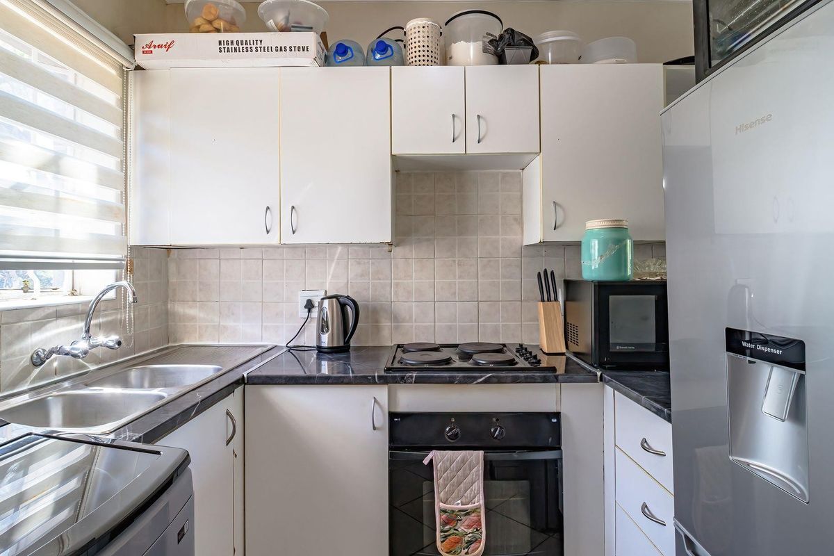 Compact kitchen featuring white cabinetry, dark laminate countertops, a double basin sink, and a built-in electric oven with hob.