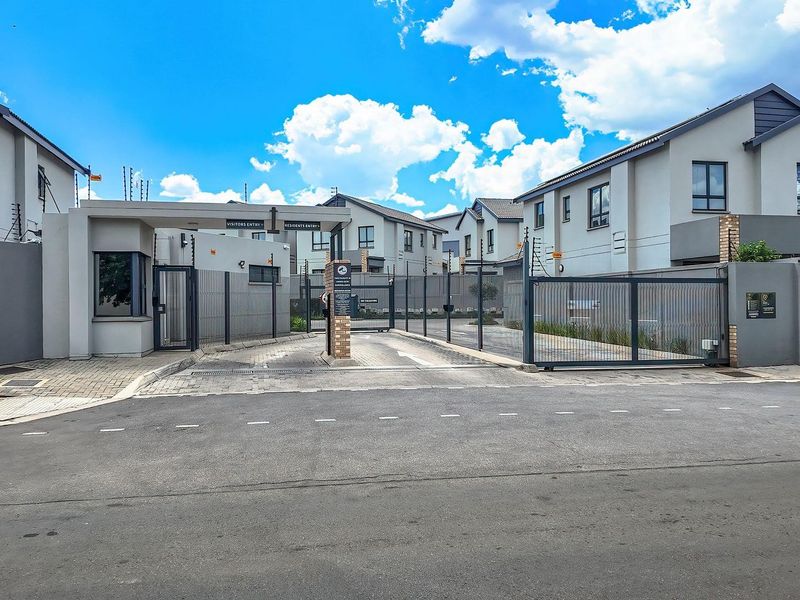 Street view of the secure entrance to Olea View Houses, featuring a gated access point, electric fencing, and modern perimeter walling.